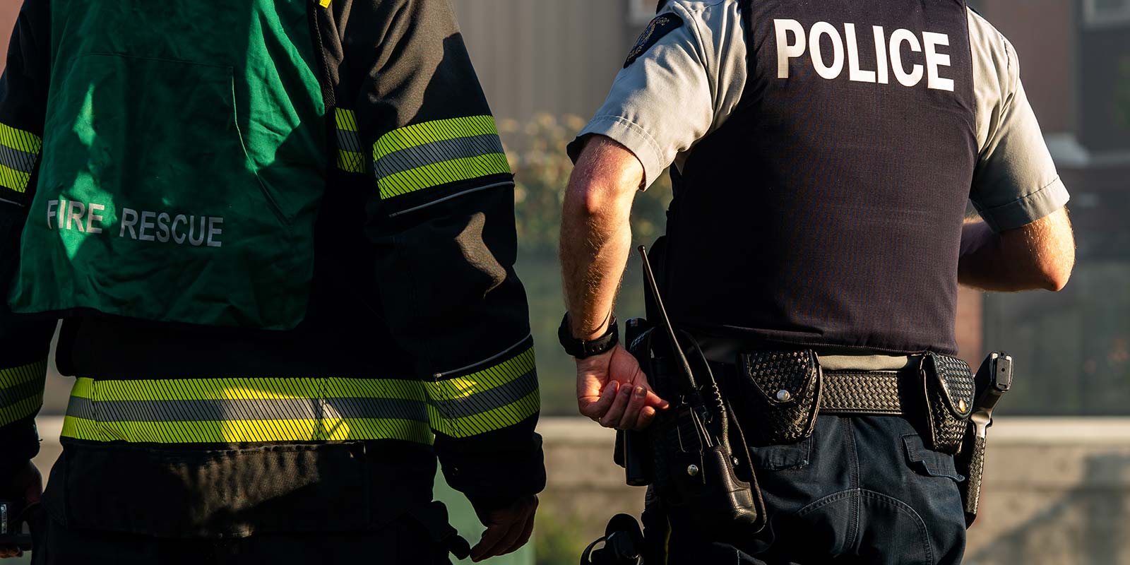 a policeman and fire fighter, backs turned to viewer, at the scene