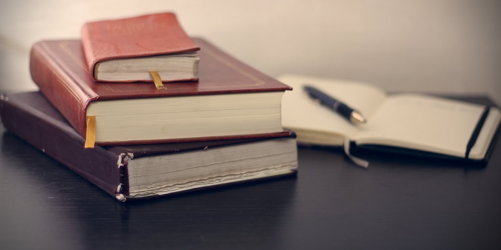 stack of academic looking books and an open notebook on a desk