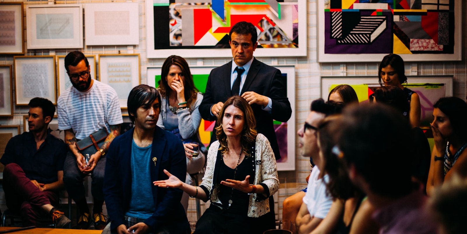 Group of over 14 people together in a meeting room, one woman speaking