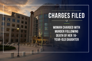 Graphic announcing criminal charges by the First Judicial District Attorney's Office. The background shows the Jefferson County Administration and Courts Building at dusk with a dark navy gradient overlay. At the top, the headline reads "Charges Filed." Large text states: "WOMAN CHARGED WITH MURDER FOLLOWING DEATH OF HER 16-YEAR-OLD DAUGHTER"