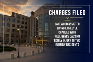 Graphic from the First Judicial District Attorney's Office for Gilpin and Jefferson Counties announcing criminal charges. The left half of the image shows the Jefferson County courthouse at dusk. The right half features a dark blue overlay with the District Attorney's Office seal and the headline "Charges Filed." Below, large white text reads: "Lakewood Assisted Living Employee Charged with Negligence Causing Bodily Injury to Two Elderly Residents." A thin white border frames the graphic.