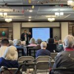 District attorney presenting to a large crowd of seated seniors.